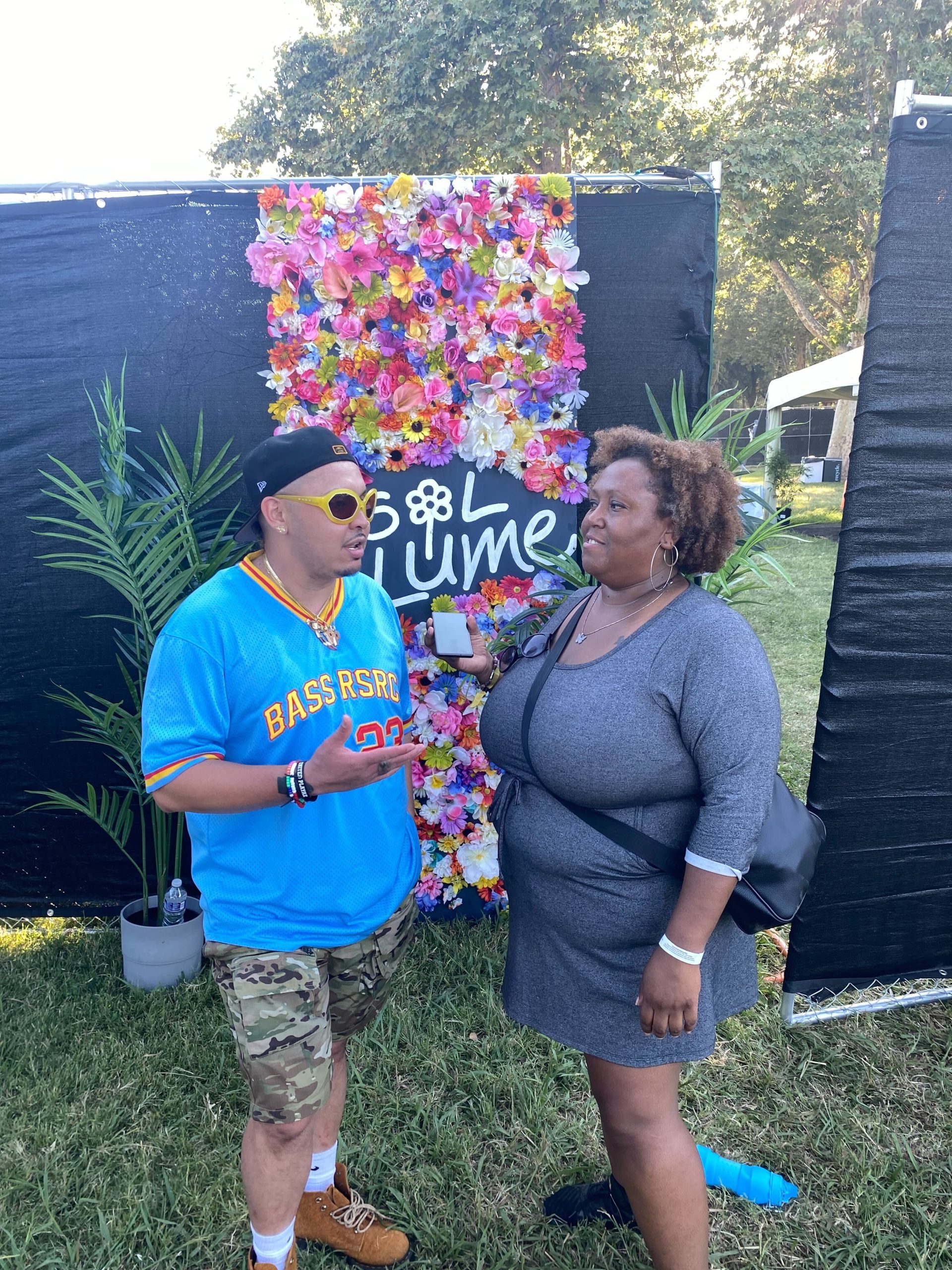 An African American woman in a dress interviews a Pilipino man in shades and a backwards cap