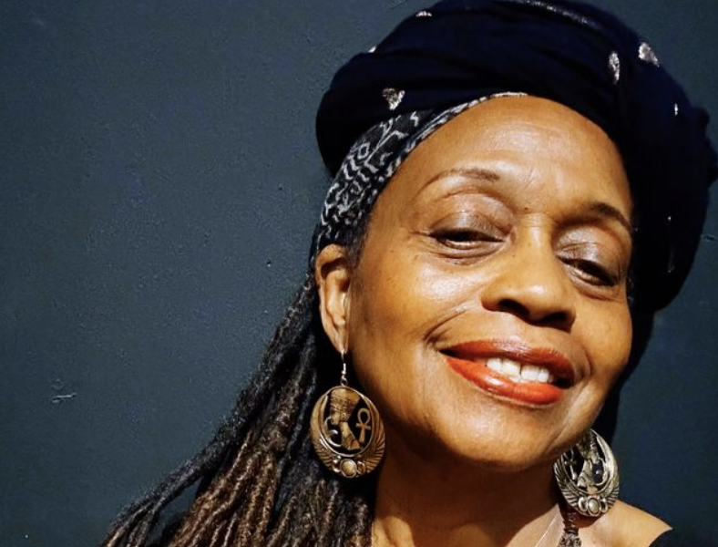 A Black woman wearing a black hat smiles at camera