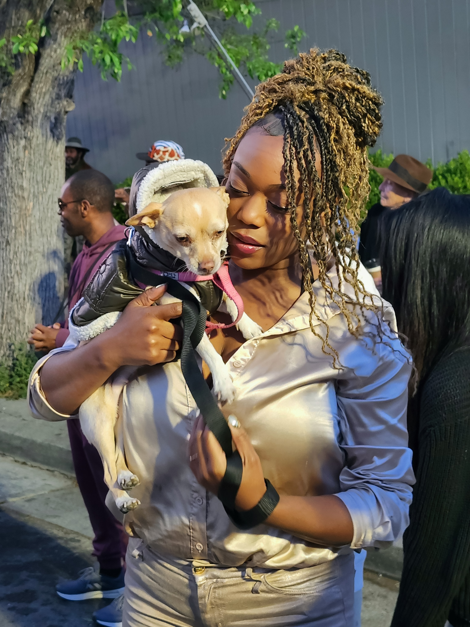 An African American woman holds up a small sandy colored chihuahua
