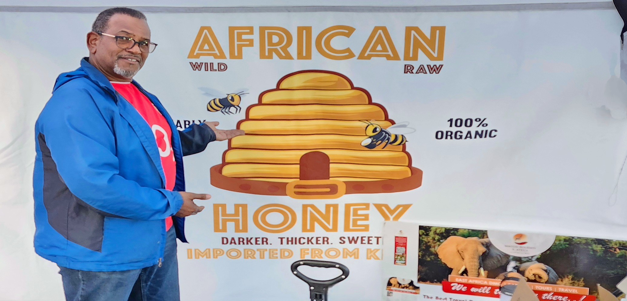 An African American man stands in front of a white banner that says African Honey