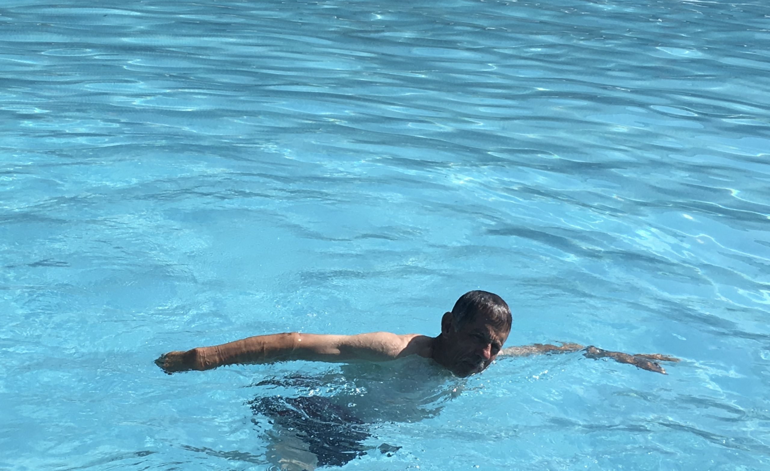 a Latino man swimming in a pool with arms extended