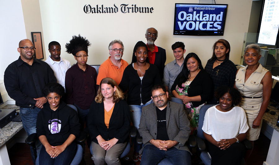 a group of diverse people pose for a photo in front of The Oakland Tribune sign