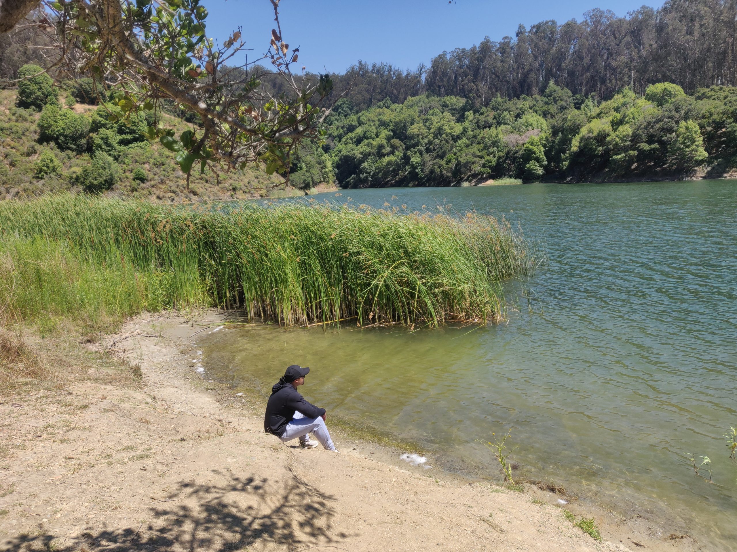 A man sits near an emerald colored lake