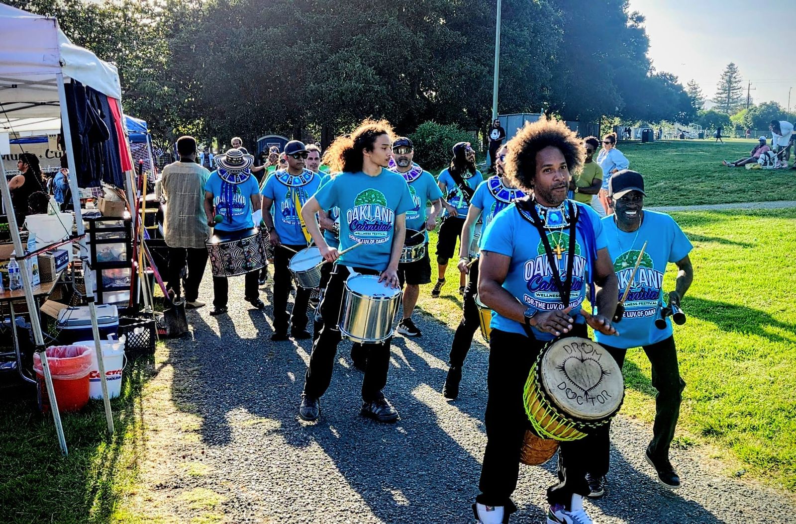 SambaFunk! drummers wearing blue shirts perform near vendor booths during the Malcolm X JazzArts Festival in Oakland.